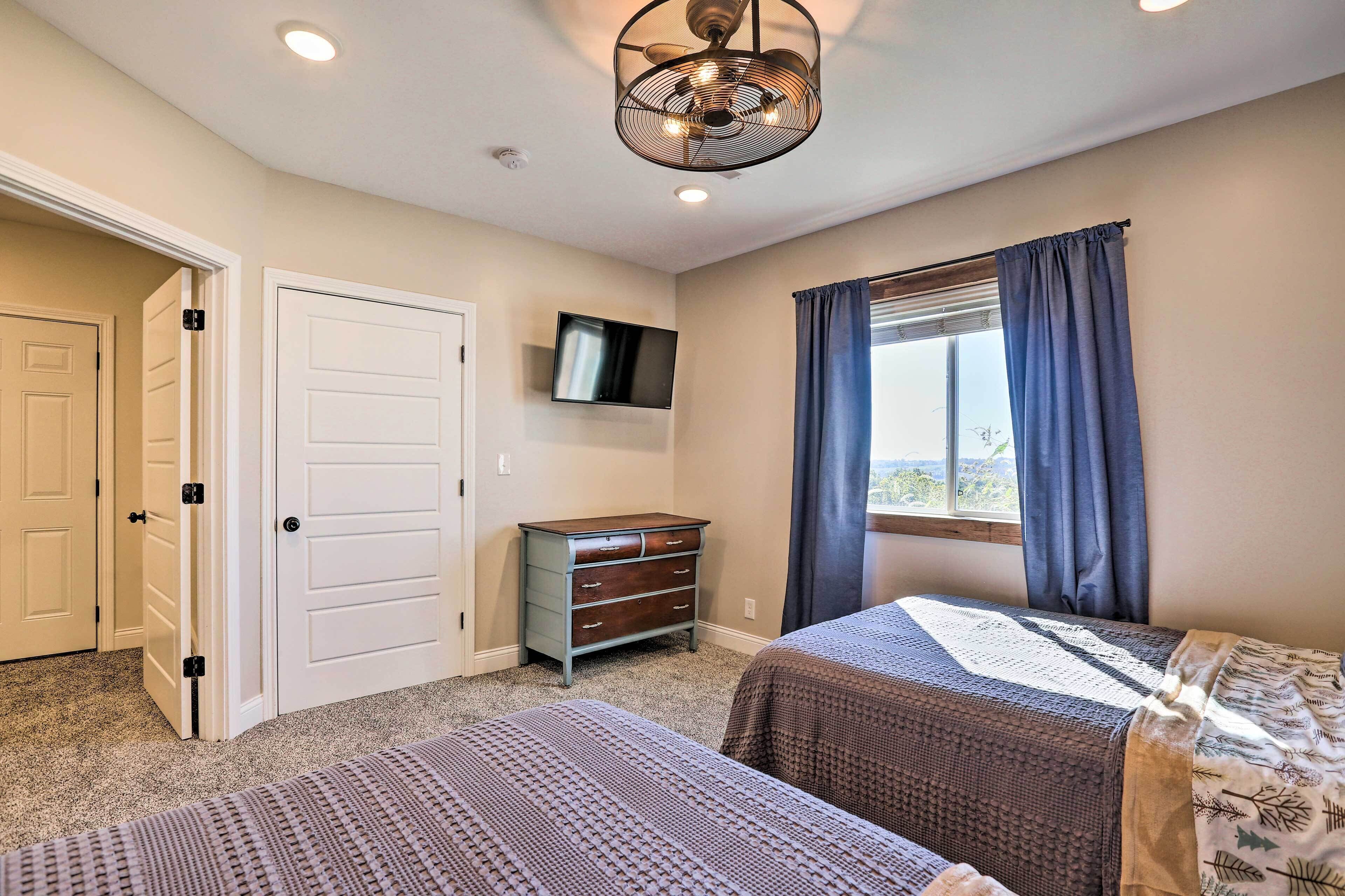 A bedroom with two beds, a dresser, a TV, and a window with curtains.