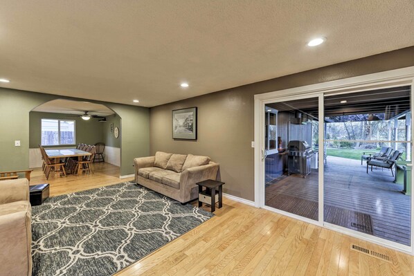 A spacious living room with a large sofa, a dining area, and a sliding glass door leading to an outdoor deck.
