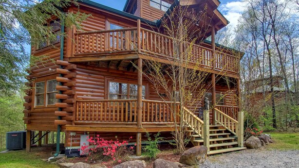 Une cabane en rondins dotée d’une terrasse en bois et d’un escalier menant à un balcon.