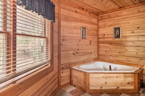 Ein Badezimmer in einer Holzhütte mit einer großen Badewanne, Holzwänden und einem Fenster mit Jalousien.