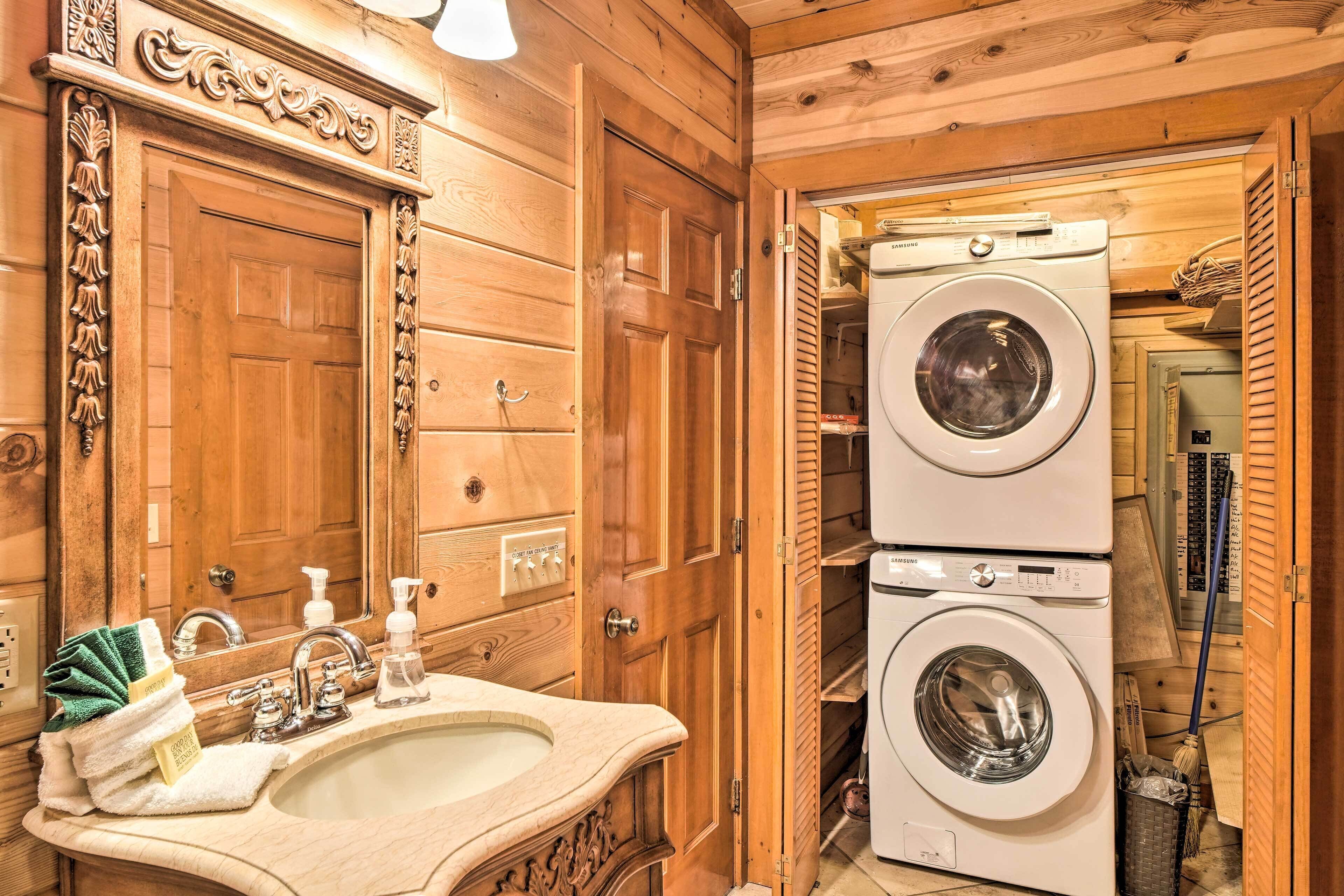 Un baño con piso y muebles de madera, un lavabo, un espejo y lavadoras apiladas.