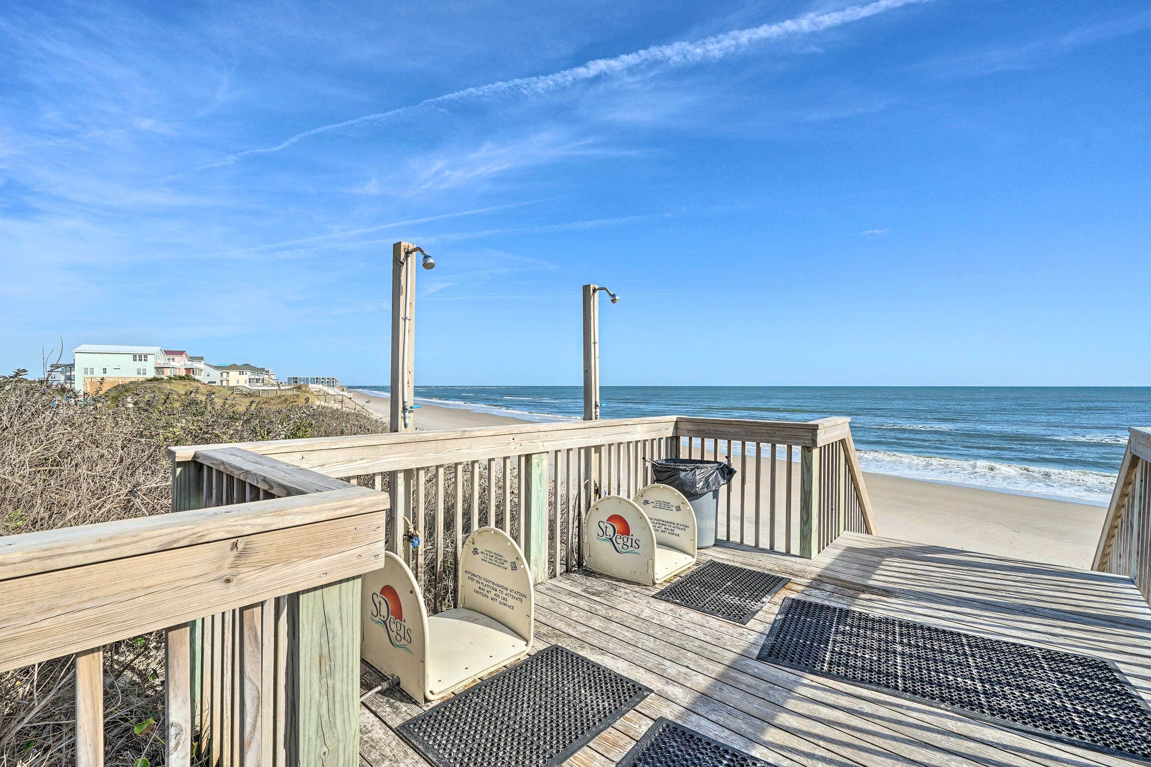 Terraza de madera con vista a la playa y al océano, incluyendo sillas de playa y botes de basura.