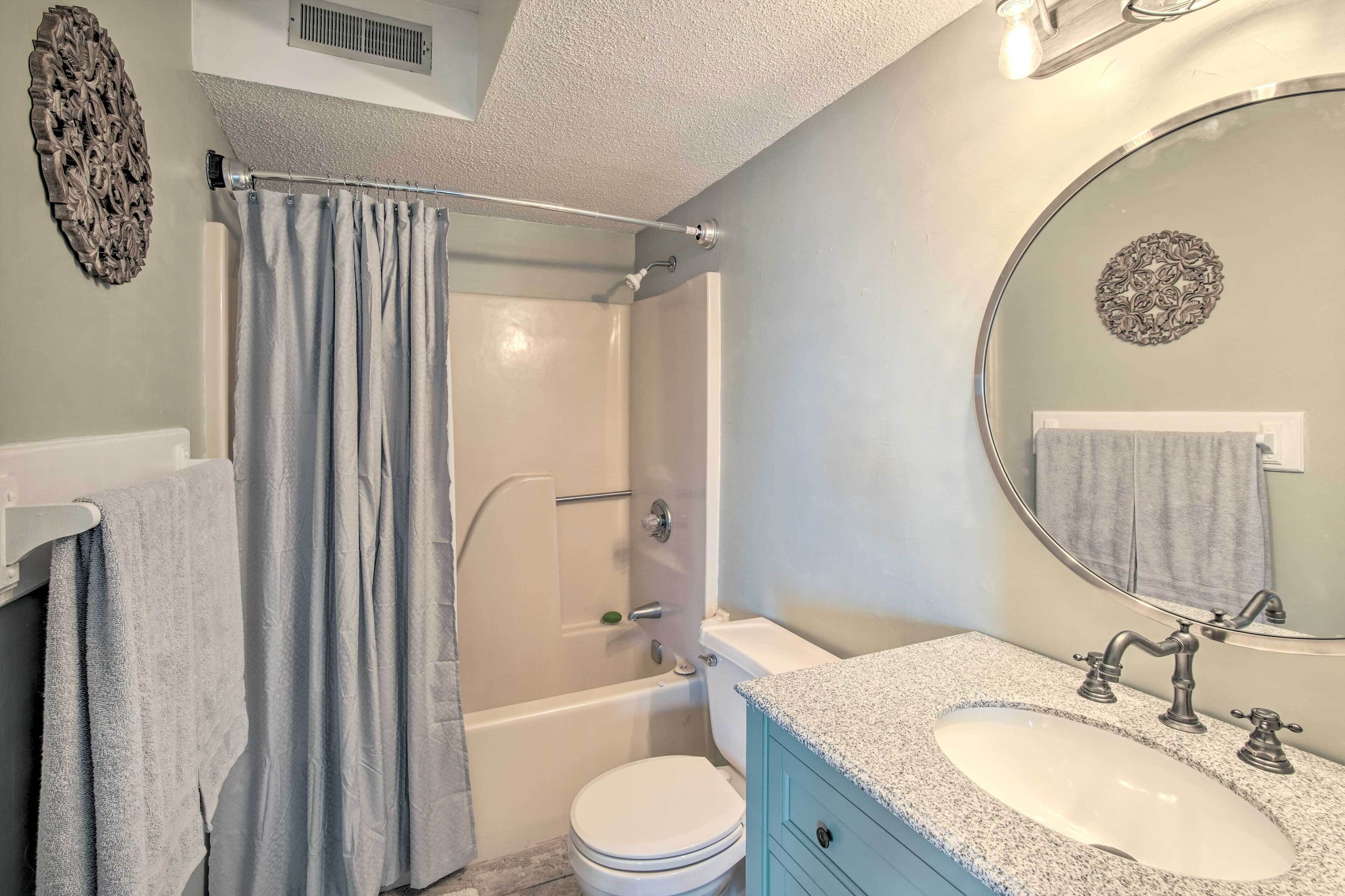 A bathroom with a shower, toilet, sink, and a mirror.