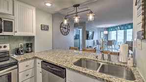 A kitchen with granite countertops, stainless steel appliances, and a modern light fixture. - Colorful Beachfront Condo w/ Resort Amenities (Sneads Ferry)