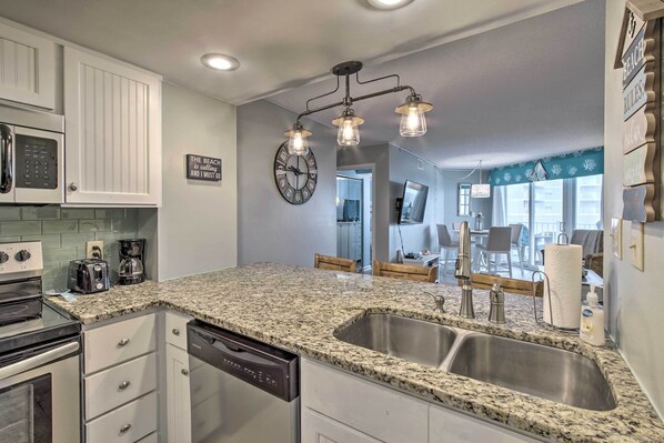 A kitchen with granite countertops, stainless steel appliances, and a modern light fixture. - Colorful Beachfront Condo w/ Resort Amenities (Sneads Ferry)