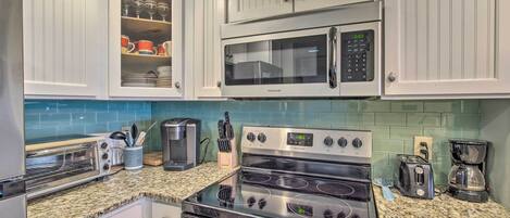 A kitchen with white cabinets, a microwave, a stove, a toaster, and a coffee maker.