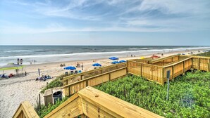 A beach with wooden walkways, umbrellas, and a sandy shore. - Colorful Beachfront Condo w/ Resort Amenities (Sneads Ferry)
