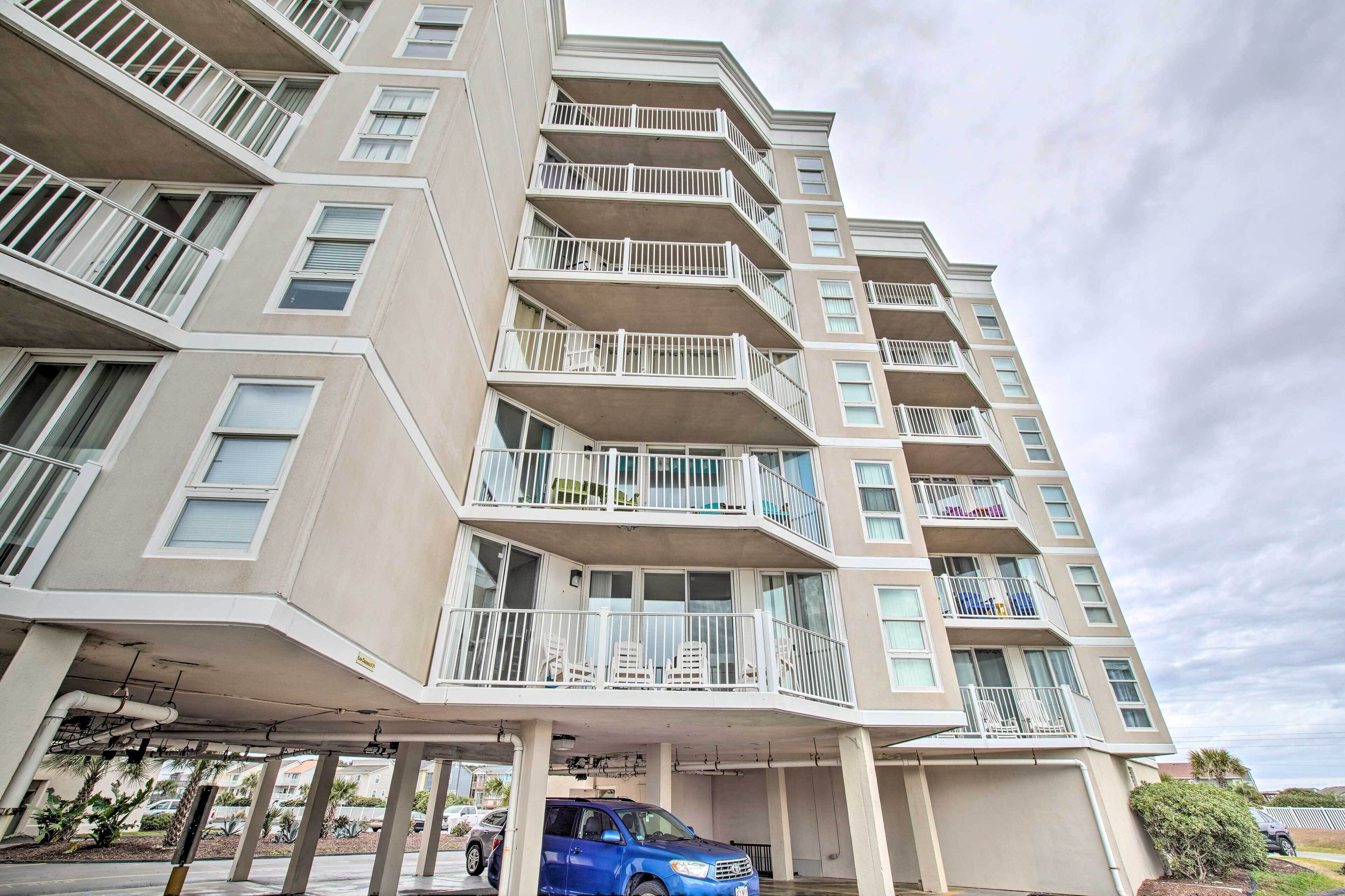 A multi-story residential building with balconies, a parking garage, and a blue SUV parked in the garage.