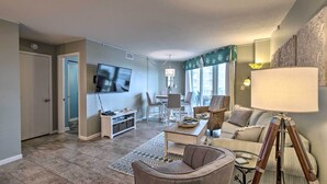 A living room with a television, a coffee table, and a sofa. There is a door leading to another room. - Colorful Beachfront Condo w/ Resort Amenities (Sneads Ferry)
