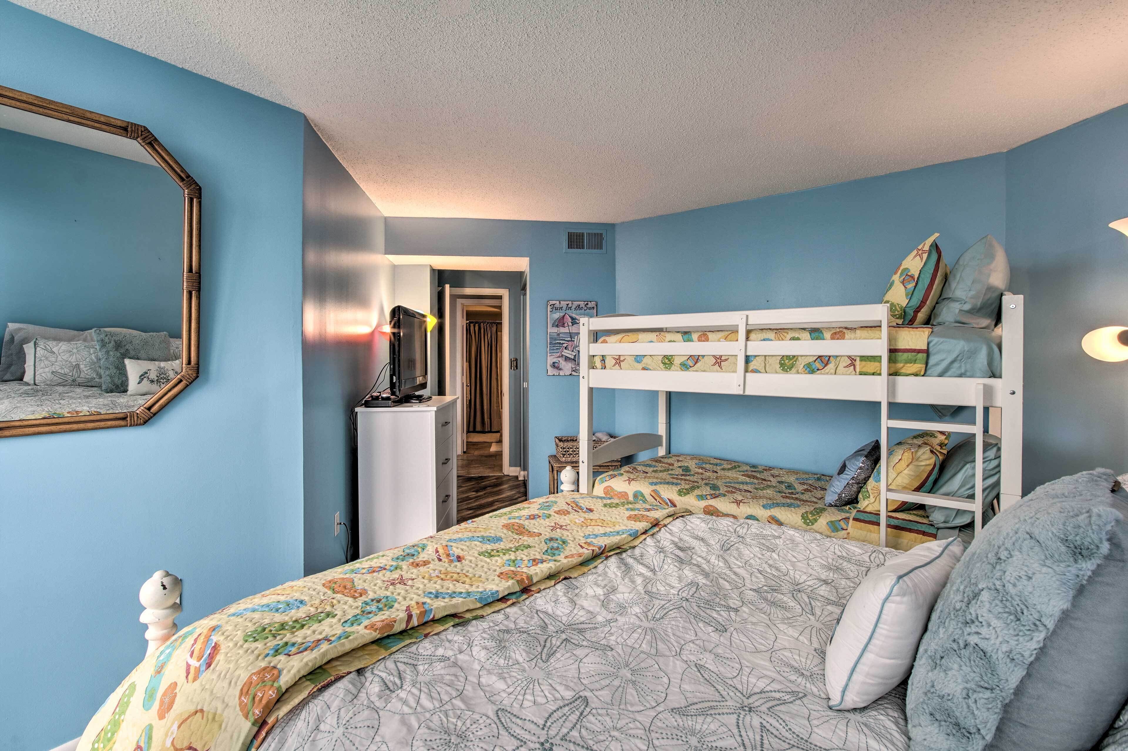 Ein Schlafzimmer mit Etagenbett, Kommode, Spiegel und einer Tür zu einem anderen Raum.