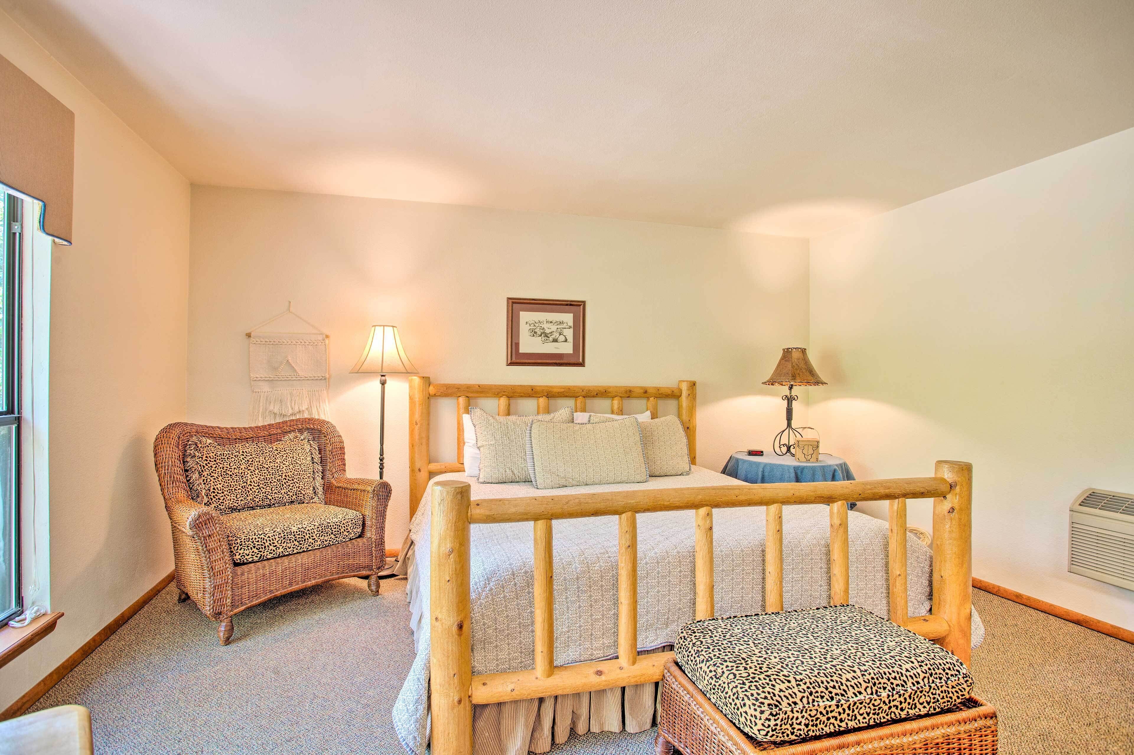 A cozy bedroom with a wooden bed, a wicker armchair, and a small table with a lamp.