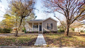 A single-story house with a front porch, a pathway leading to the door, and a small yard with trees and fallen leaves. - Charming Huntsville Home w/ Deck! (Huntsville)