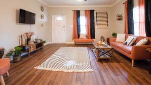 A living room with a flat-screen TV, a ceiling fan, a sofa, a coffee table, and a large rug. - Charming Huntsville Home w/ Deck! (Huntsville)