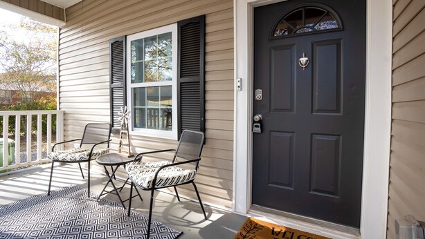 A front porch with a dark door, two chairs, a patterned rug, and a welcome mat. - Charming Huntsville Home w/ Deck! (Huntsville)