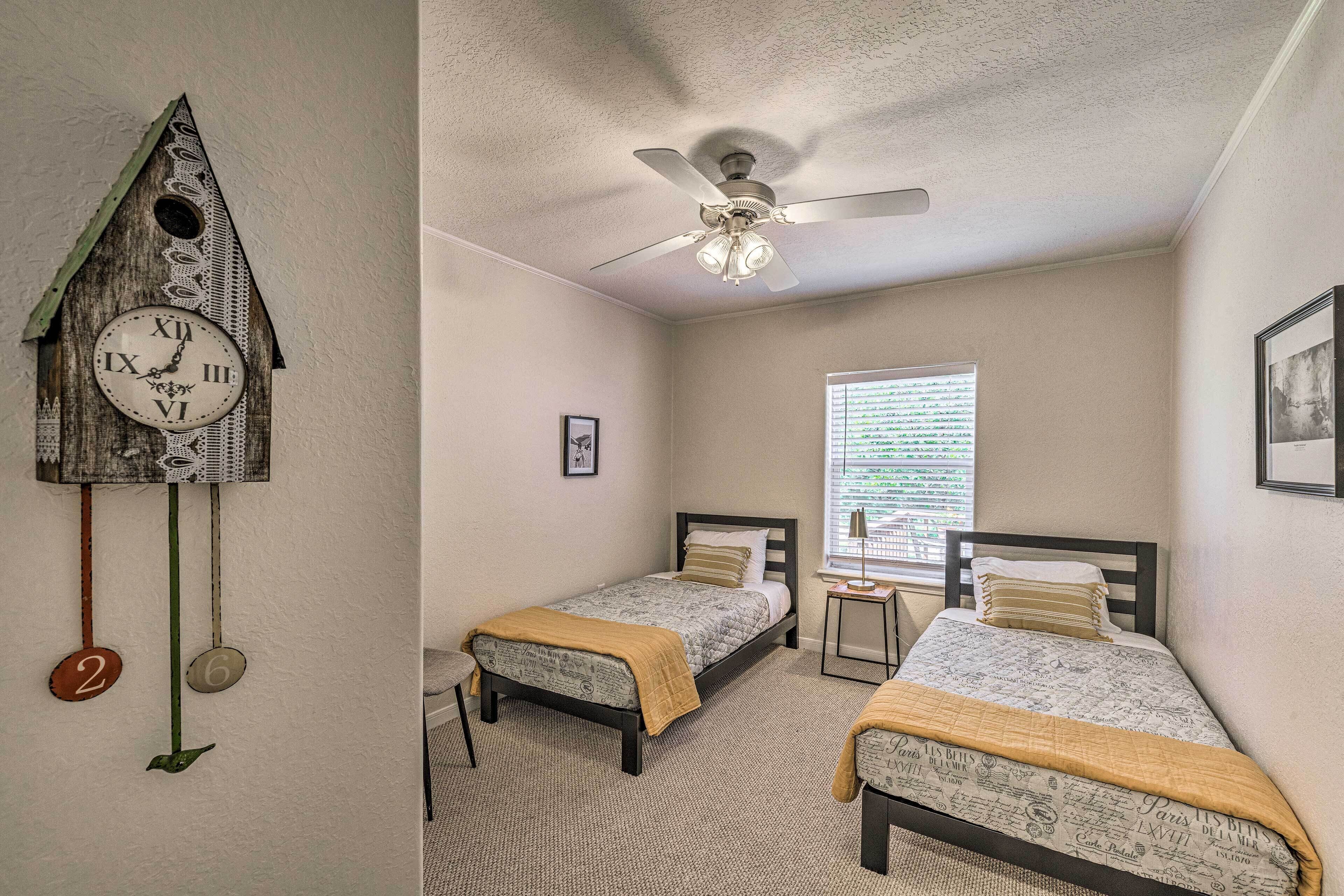 A bedroom with two beds, a ceiling fan, and a wall clock.