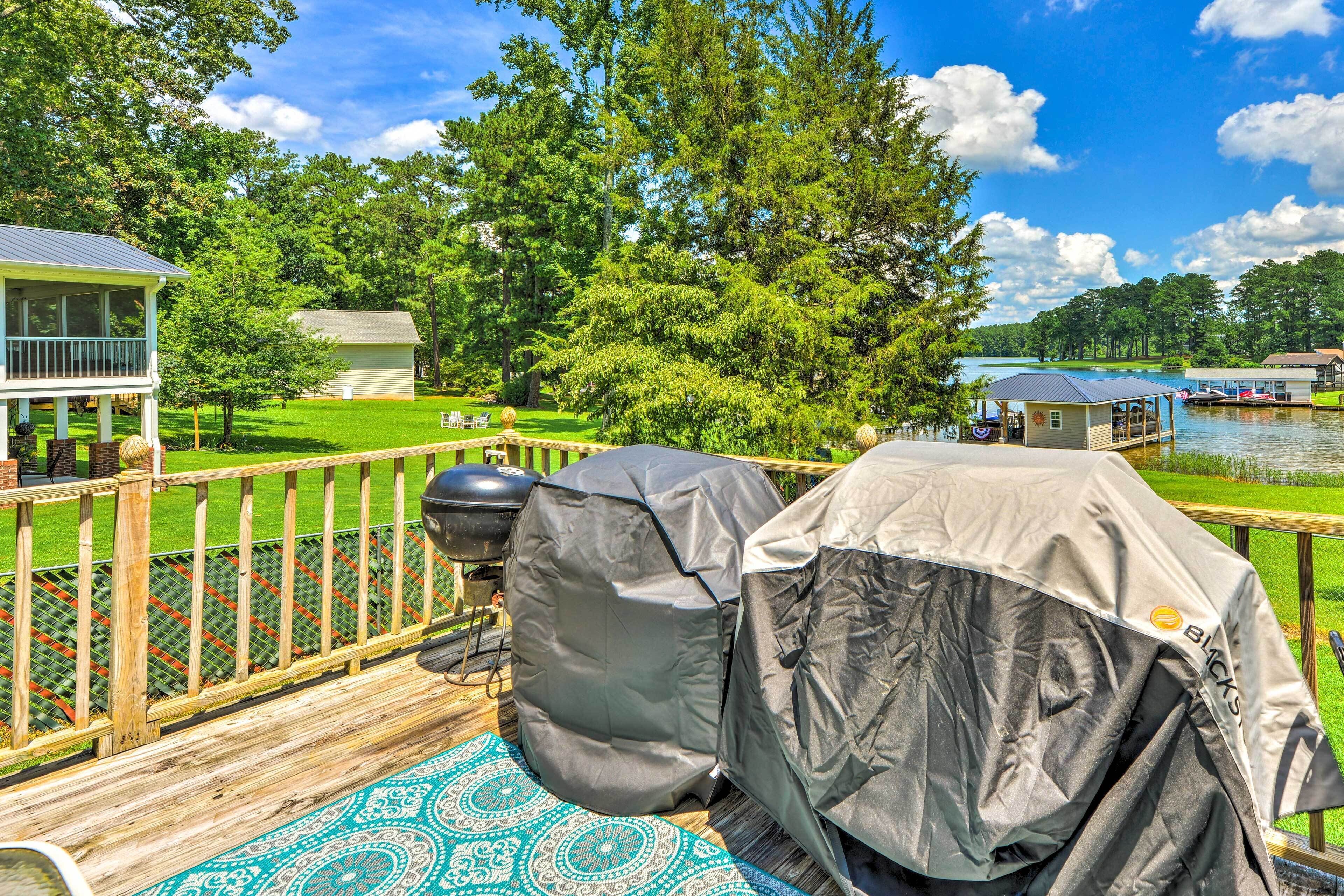 A deck with barbecue grills, a covered tent, and a view of a lake and buildings.
