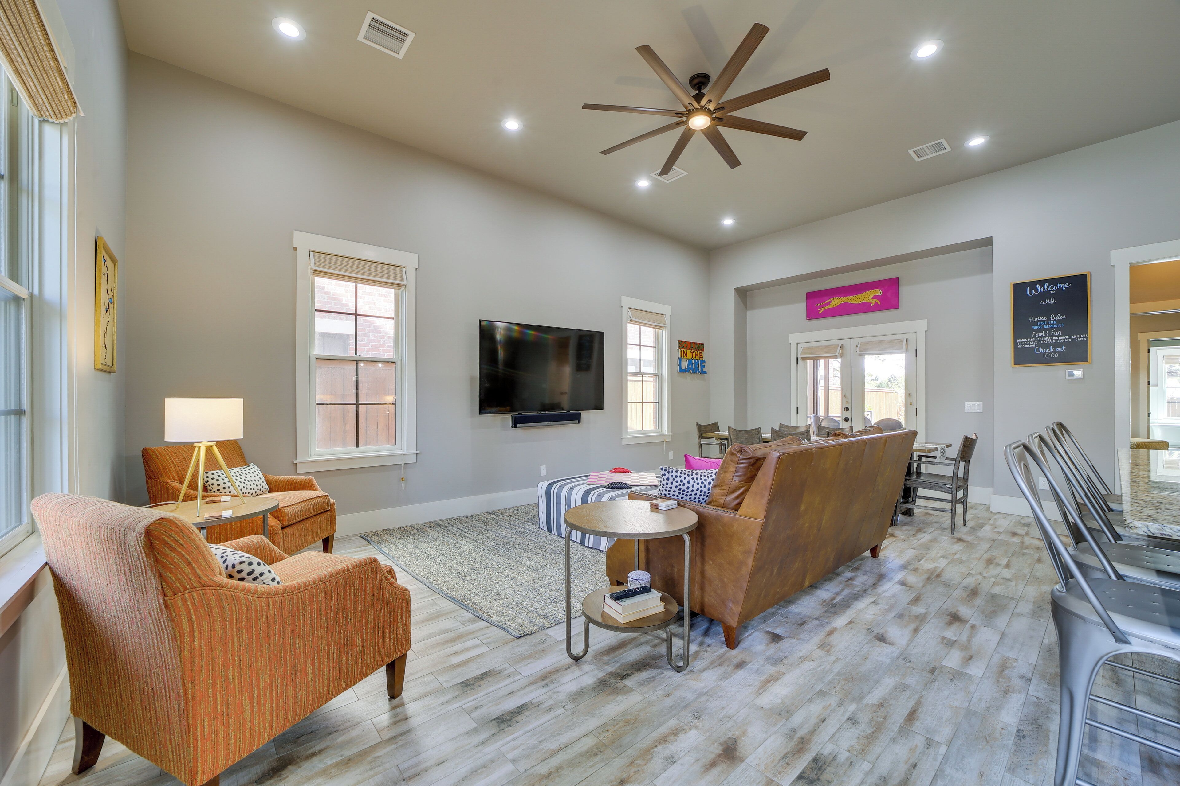 A spacious living room with a ceiling fan, a flat-screen TV mounted on the wall, and a dining area with a long table and chairs.