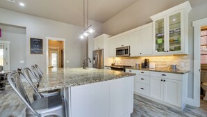 A modern kitchen with white cabinets, granite countertops, stainless steel appliances, and a bar seating area. - Carlton Landing Retreat w/ Eufaula Lake Access! (Eufaula)