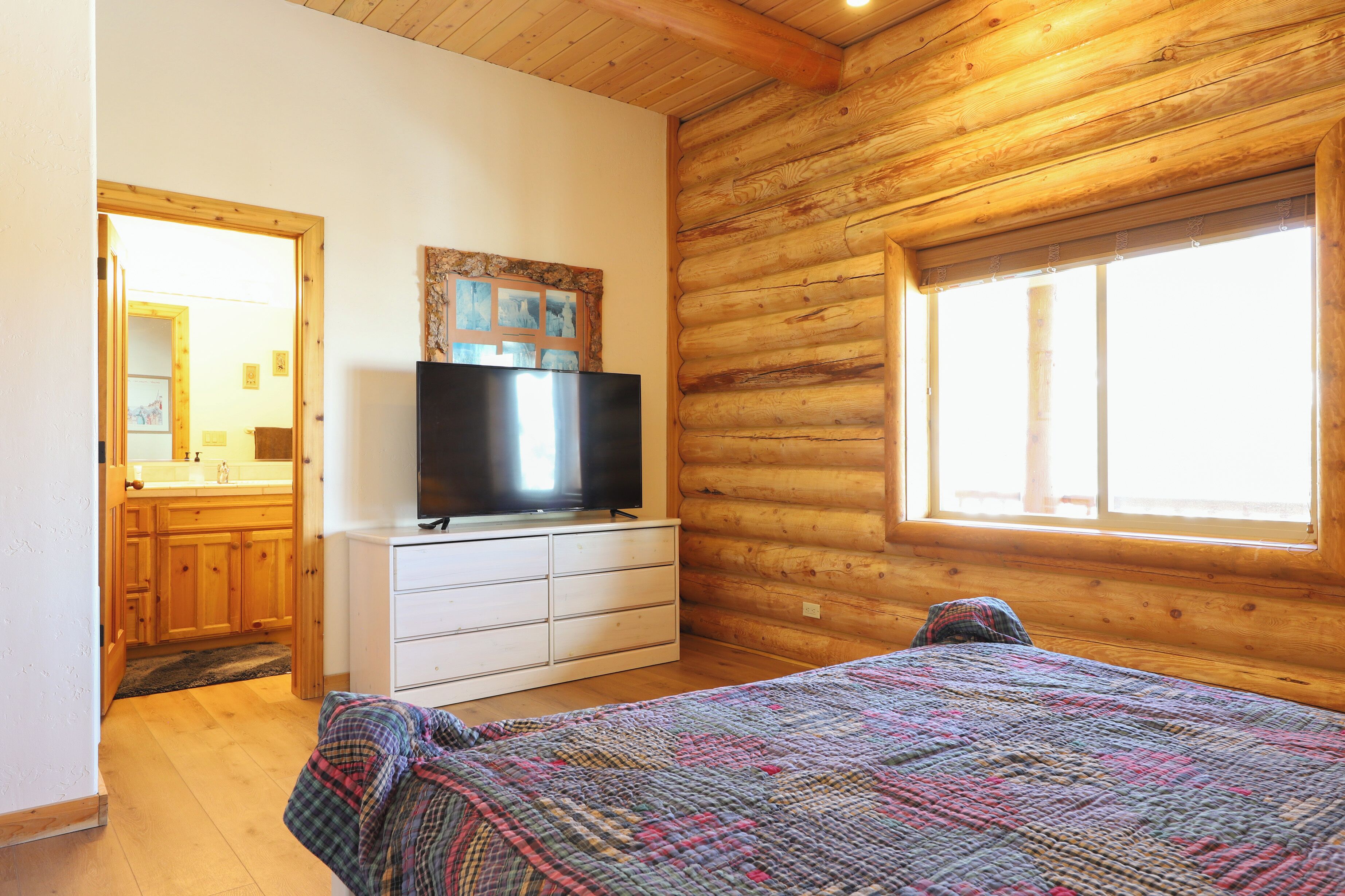 Une chambre dans un chalet en rondins, avec un lit, un téléviseur posé sur une commode, des murs en bois et une fenêtre.