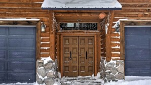 En stuga byggd av trä med en grund av sten, en centralt placerad trädörr och två garageportar.