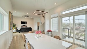 A spacious kitchen with a large island, a dining area with chairs, and a view of the outdoors through large windows. - Downtown Houston Townhome w/ Balcony + Yard! (Houston)