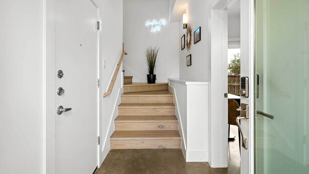 A staircase with wooden steps leading to a landing with a neon sign, white walls, and a glass door on the right. - Downtown Houston Townhome w/ Balcony + Yard! (Houston)
