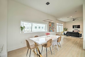Uma sala ampla com mesa de jantar, cadeiras, um sofá preto e uma TV fixada na parede.