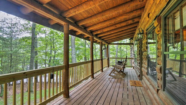A wooden deck with a railing, a rocking chair, and a window overlooking a forest.