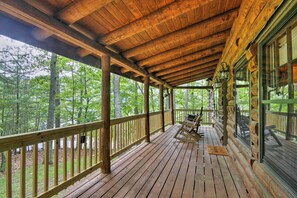 Eine Holzterrasse mit Geländer, einem Schaukelstuhl und einem Fenster mit Blick auf einen Wald.