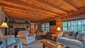 A cozy log cabin interior with a stone fireplace, comfortable seating, and large windows.