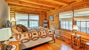 A log cabin bedroom with a bed, windows, and a lamp.