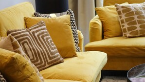 A yellow sofa with patterned cushions, a black lamp, and a window with curtains.