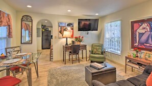 A spacious living room with a glass dining table, a green armchair, a flat-screen TV mounted on the wall, and a large painting on the wall. - Cozy 'mona Lisa Villa - Near Downtown Hot Springs (Hot Springs)