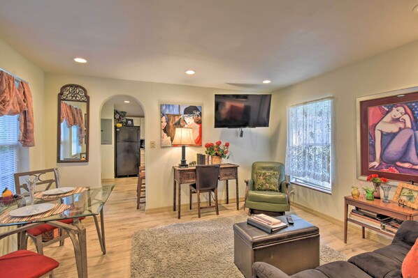 A spacious living room with a glass dining table, a green armchair, a flat-screen TV mounted on the wall, and a large painting on the wall. - Cozy 'mona Lisa Villa - Near Downtown Hot Springs (Hot Springs)