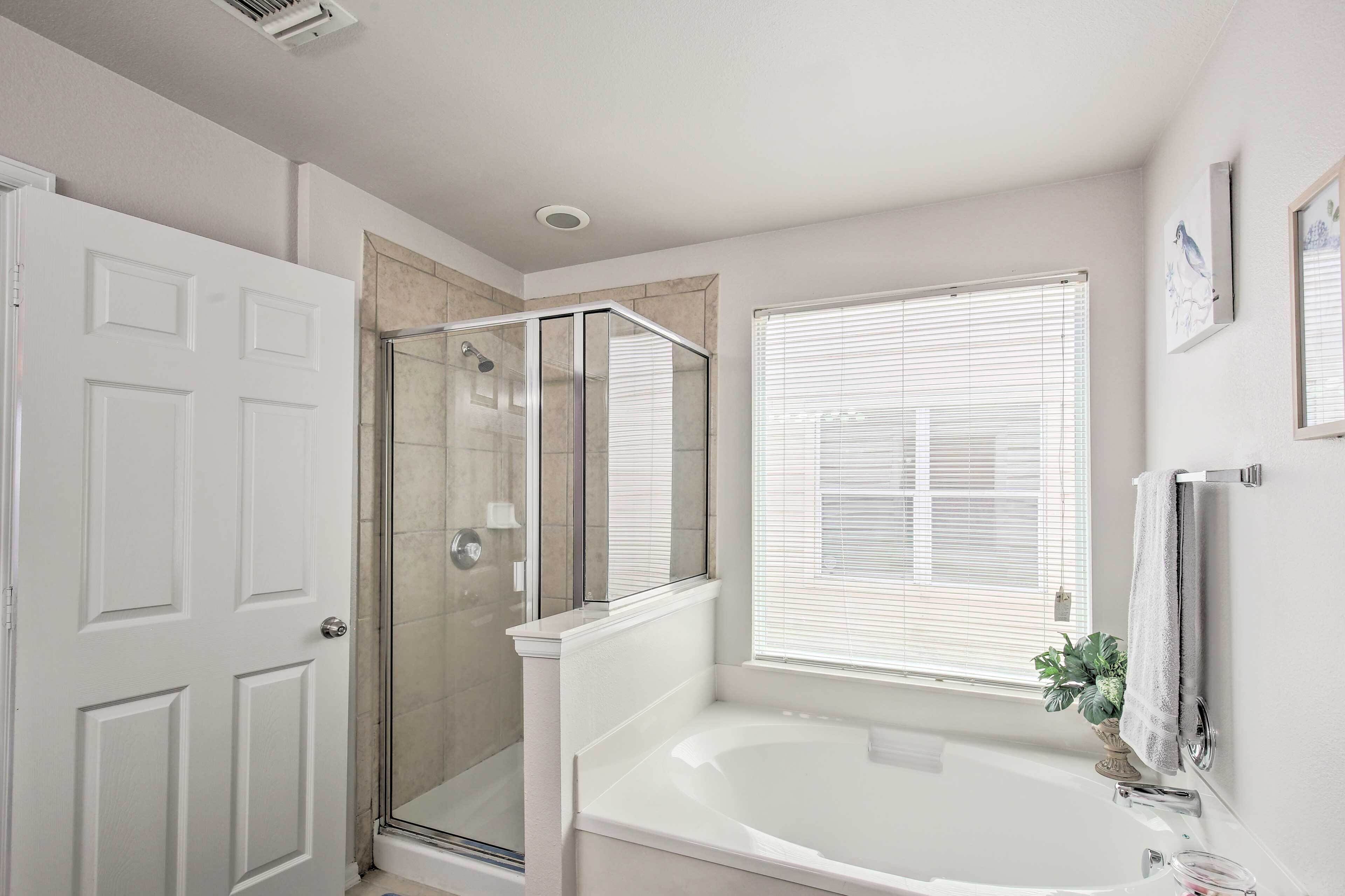 A bathroom with a glass-enclosed shower, a bathtub, and a window with blinds.