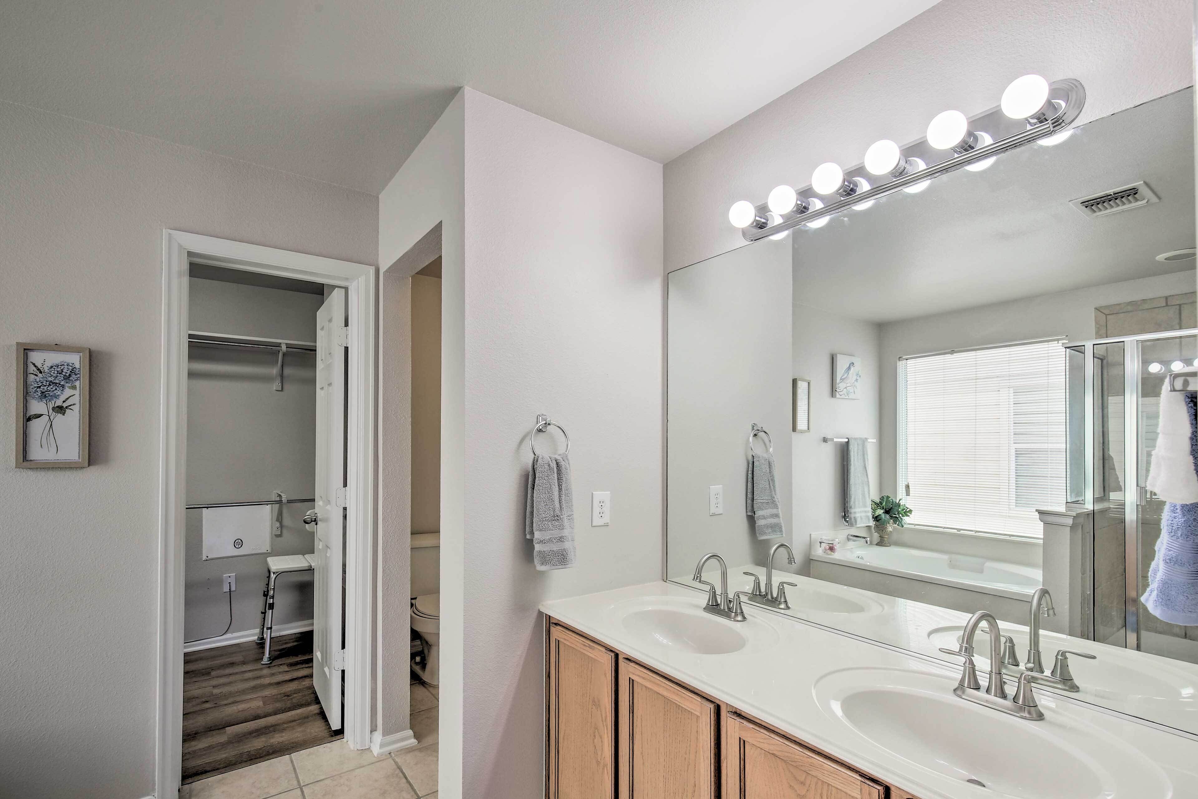 A modern bathroom with a large mirror, dual sinks, and a walk-in closet.