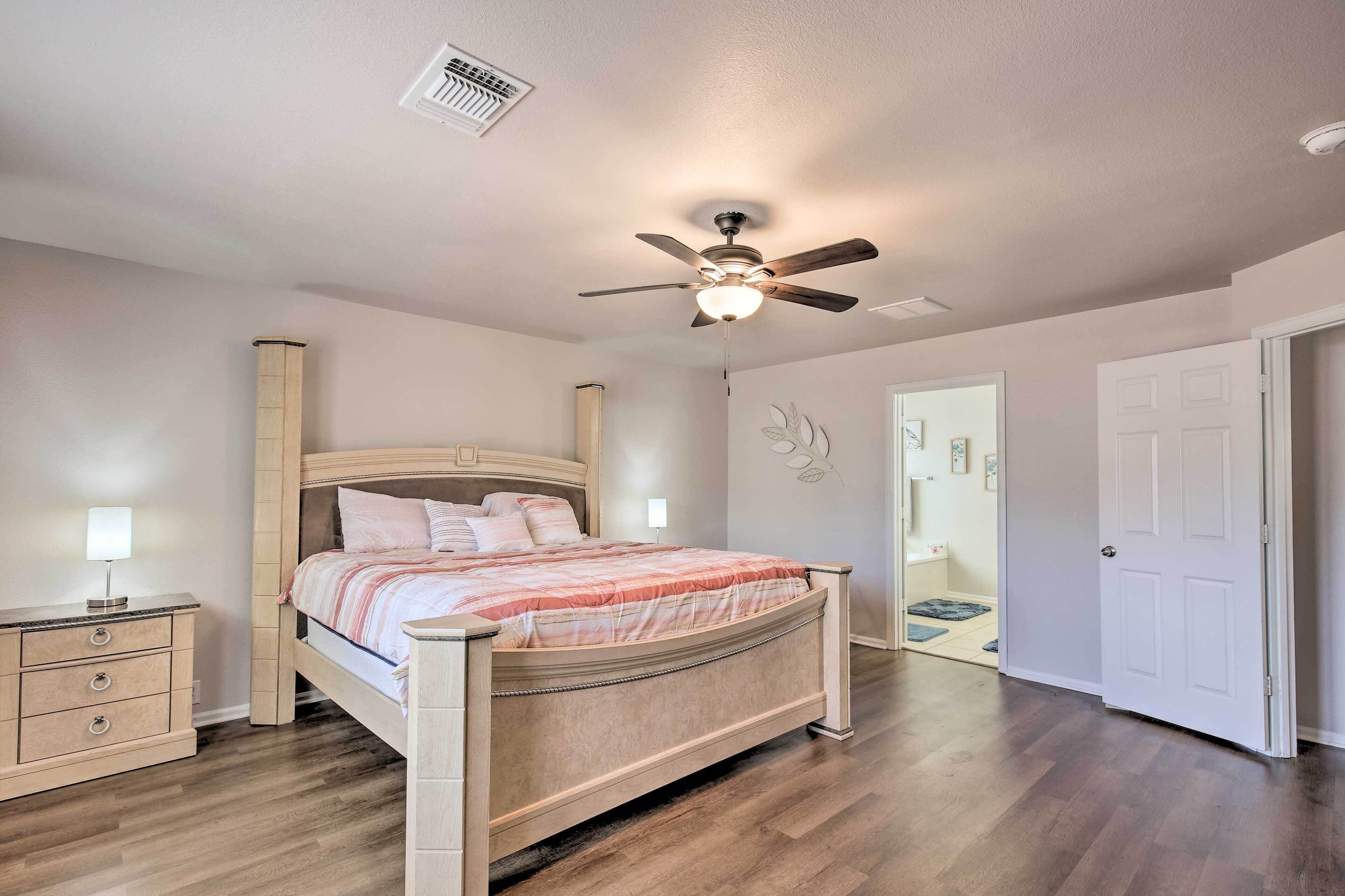Quarto com cama de madeira, mesa de cabeceira, ventoinha no teto e porta branca.