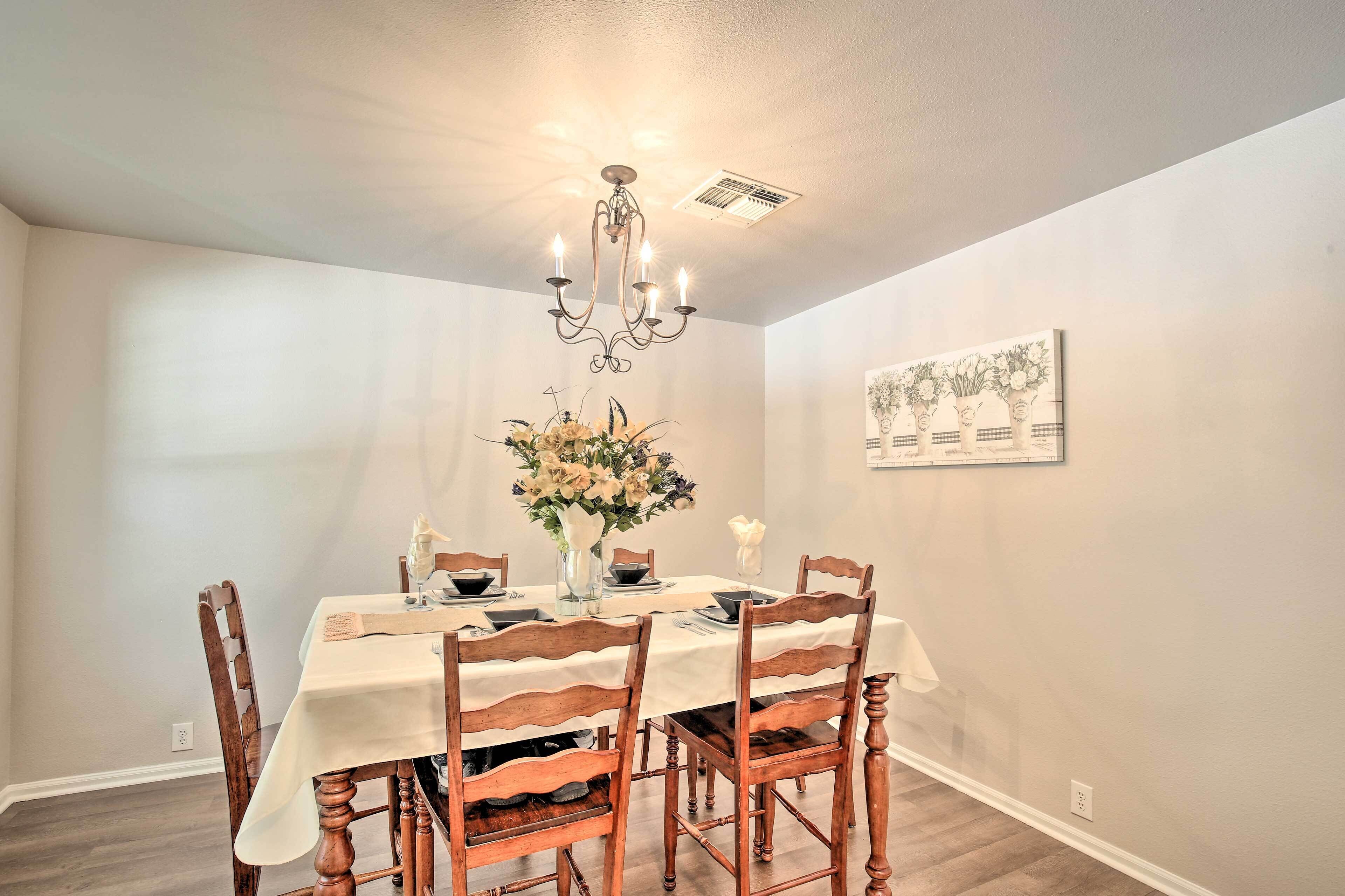 A dining room with a chandelier, a table set for four, and a floral centerpiece.