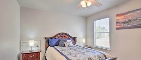 A bedroom with a bed, nightstands, a ceiling fan, a window with blinds, and a painting on the wall.