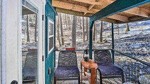 A covered outdoor seating area with two chairs and a table, overlooking a snowy forest. - Hiking Trails On-site: Cozy Falls Brook Cabin (Brattleboro)