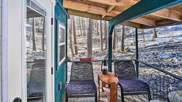 A covered outdoor seating area with two chairs and a table, overlooking a snowy forest.