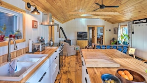 A kitchen with wooden beams, a large island, and a dining area with blue upholstered chairs. - Hiking Trails On-site: Cozy Falls Brook Cabin (Brattleboro)