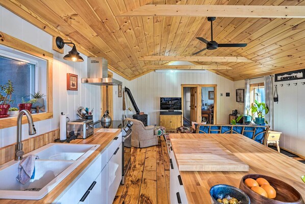 A kitchen with wooden beams, a large island, and a dining area with blue upholstered chairs. - Hiking Trails On-site: Cozy Falls Brook Cabin (Brattleboro)