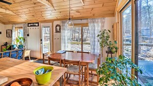 A wooden cabin interior with a dining area, large windows, and potted plants.