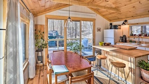 A cozy cabin interior with a wooden dining table, bar area, and large windows offering a view of the snowy outdoors. - Hiking Trails On-site: Cozy Falls Brook Cabin (Brattleboro)