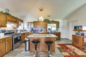 A kitchen with wooden cabinets, a stainless steel refrigerator, a microwave, a stove, and two bar stools. - Gloucester Retreat w/ Backyard Oasis & Pier! (Gloucester)