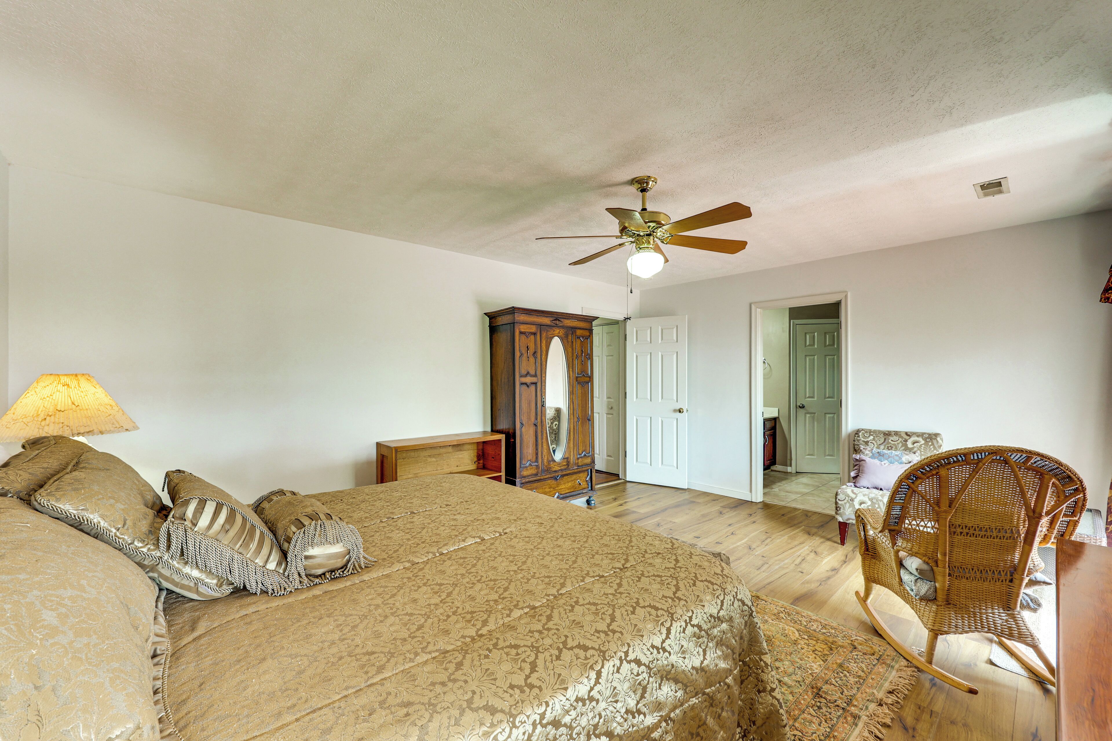 Una camera da letto con un letto, una ventola a soffitto, un comò in legno, uno specchio e una poltrona a dondolo.