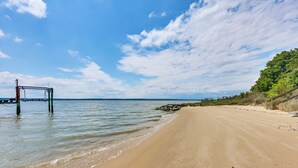 A beach with a pier extending into calm waters, a clear sky, and a sandy shore.