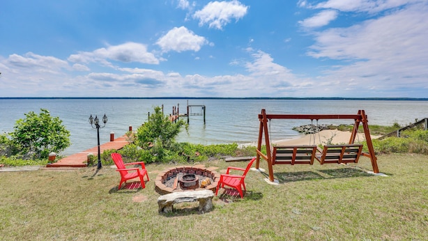 A lakeside outdoor seating area with a fire pit, red chairs, and a swing set.