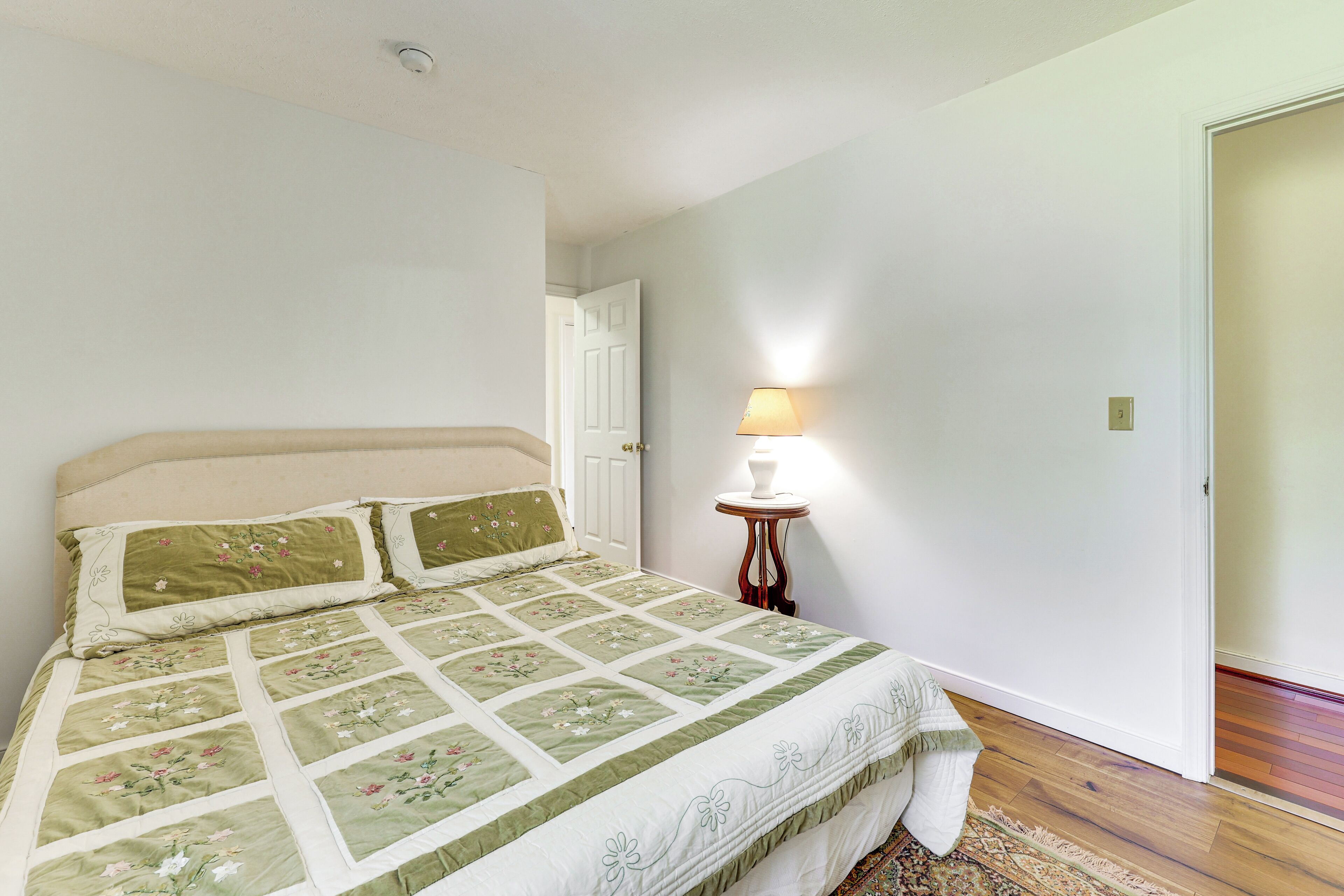 Un dormitorio con cama, una mesita de noche con lámpara y una puerta.